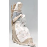 A Lladro figurine in the form of a lady seated doing embroidery. Base stamped Lladro. Measures 28 cm