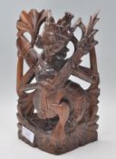 A 20th Century carved dark wood figurine of a Hindu deity Saraswati modelled seated and playing a