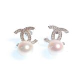 A pair of stamped 925 designer style earrings being set with white accent stones and pearl drops.