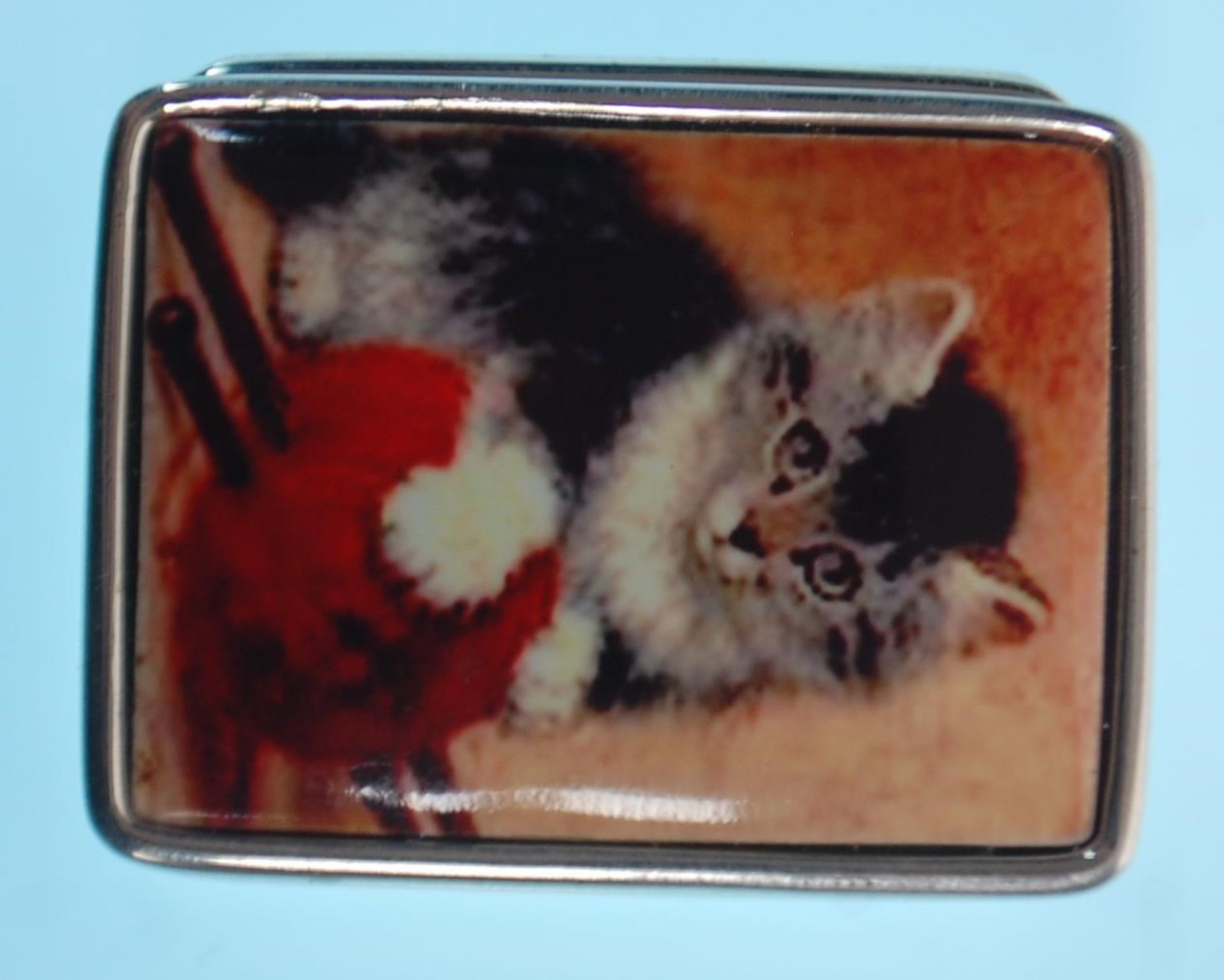 A stamped sterling silver pill box of square form having an enamelled lid with a kitten and wool