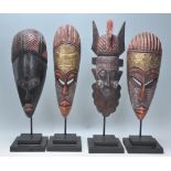A group of four carved wooden African tribal masks each being raised on supports with stepped plinth