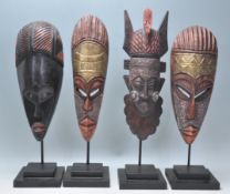 A group of four carved wooden African tribal masks each being raised on supports with stepped plinth