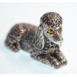 A  stamped sterling silver figurine in the form of a recumbent poodle dog with yellow glass eyes.