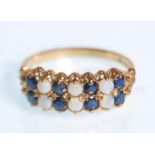 A hallmarked 9ct yellow gold ring set with opals and blue stones set to a decorative scroll mount.