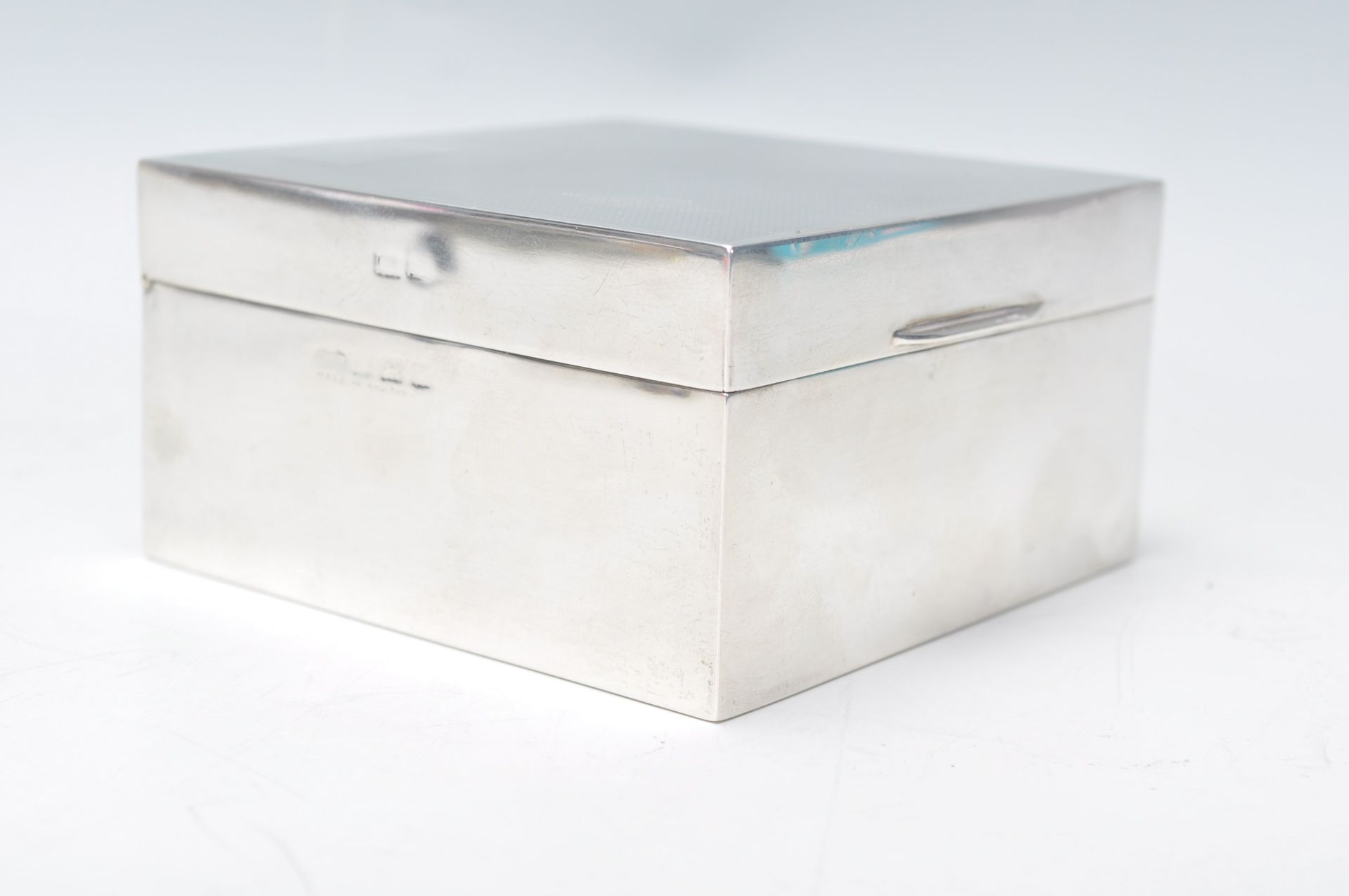 A silver hallmarked cigarette box of square form having an engine turned lid and unengraved
