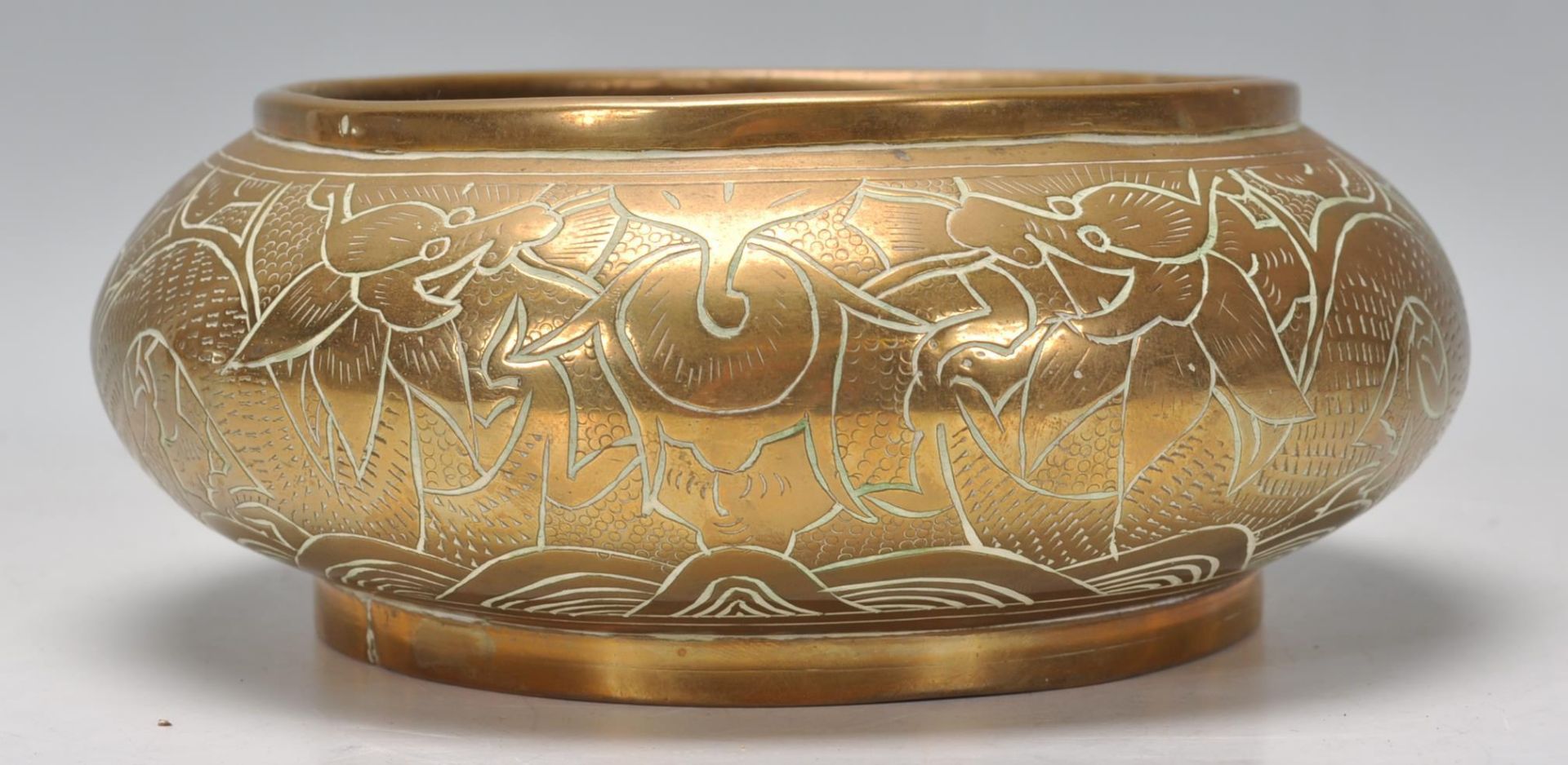 An early 20th Century bronze bowl of squat form engraved with dragons and floral decoration.