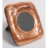 An arts and crafts style copper picture frame of square form having hammered decoration with a round