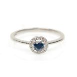 A stamped 18ct white gold ring set with a round cut sapphire and a halo of diamonds. Weight 1.8g.