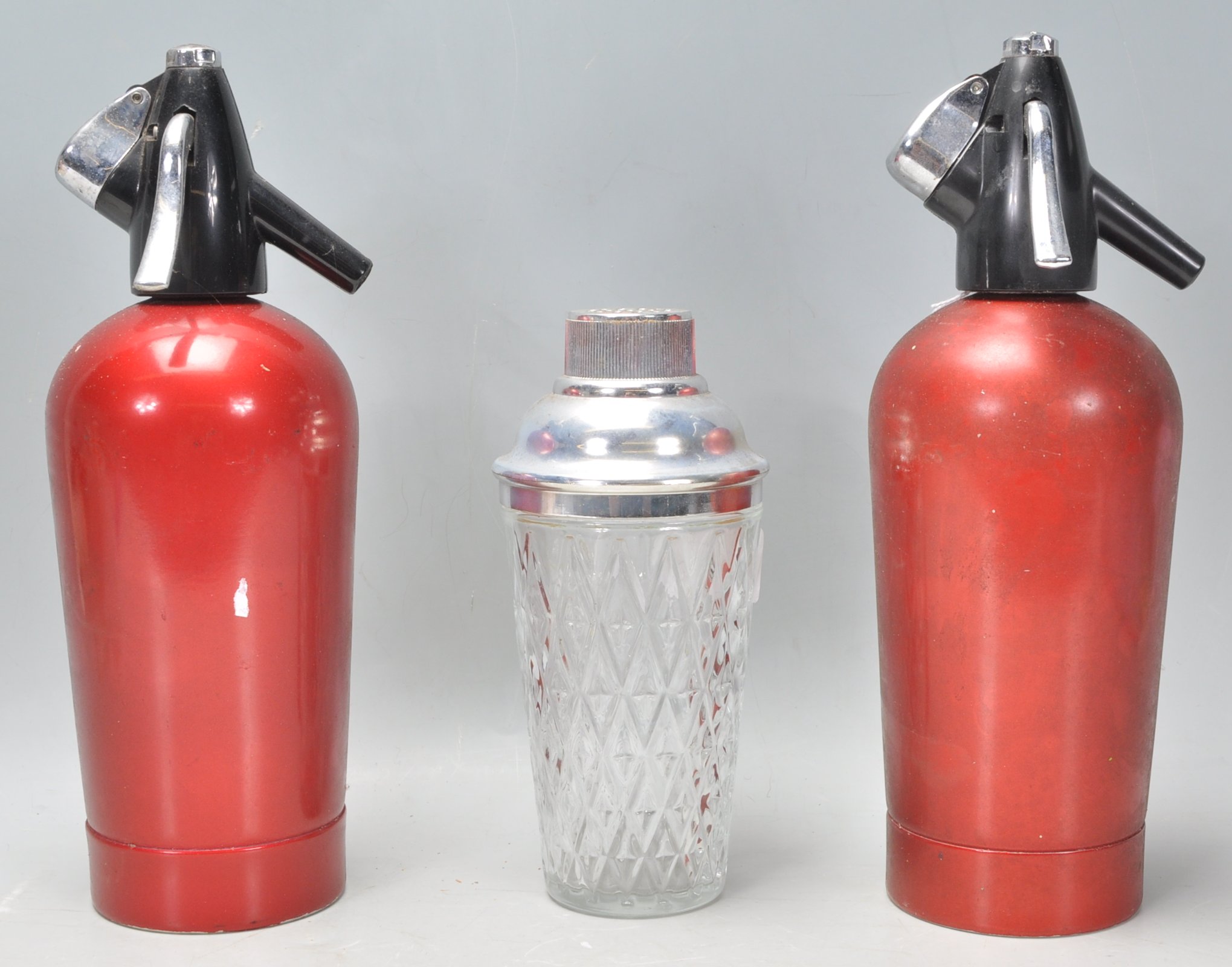A pair of vintage retro soda siphons with red metallic paint work together with a cut glass cocktail