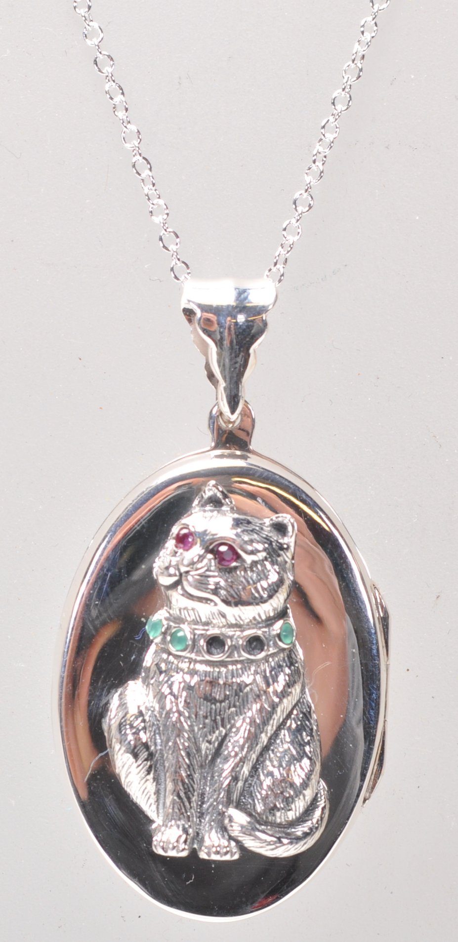 A stamped 925 silver pendant necklace having an oval locket with a raised cat wearing a collar set