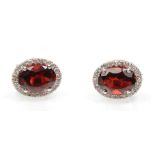A pair of 18ct white gold stud earrings set with oval cut garnets and a halo of round cut