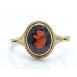 A hallmarked 9ct gold and garnet ring. The ring having an oval mixed cut garnet surrounded by a rope