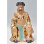 A late 19th / early 20th Century Chinese earthenware figurine in the form of a seated monk wearing a