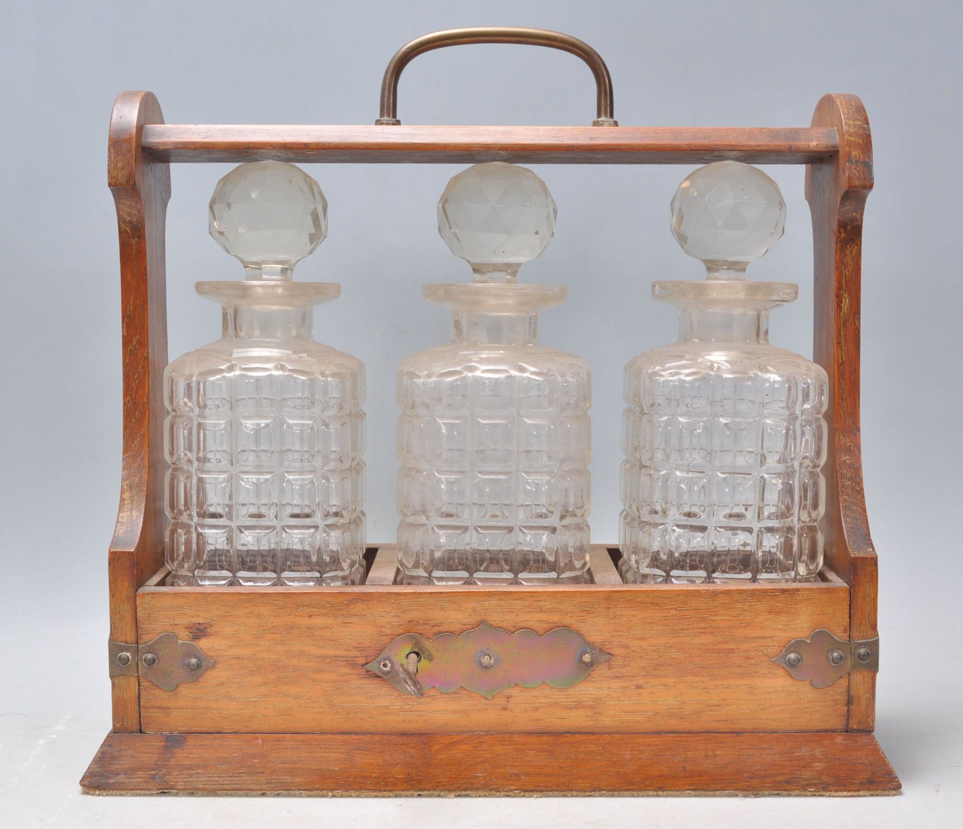 A 20th Century wooden drinks tantalus cabinet holding three cut glass decanters complete with