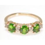 A 9ct gold diamond and green stone ring. The three oval mixed cut green stones with diamond prong