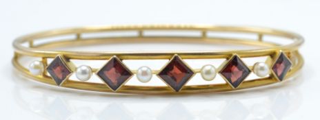 A gold pearl and garnet set bangle. The bangle set with square cut diamond garnets