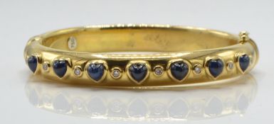 An 18ct gold sapphire and diamond bangle. The bangle set with heart shaped sapphire cabochons