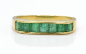 An 18ct gold and emerald ring. The ring having channel set emeralds on a raised mount