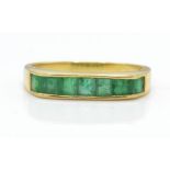 An 18ct gold and emerald ring. The ring having channel set emeralds on a raised mount