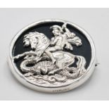 A stamped sterling silver brooch of round form having a pierced George and the dragon design set