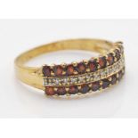 A 9ct gold garnet and diamond cluster band ring. The ring having a central band of illusion set