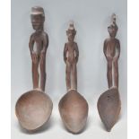 A group of three carved wooden African tribal spoons having carved figure handles and deep bowls.