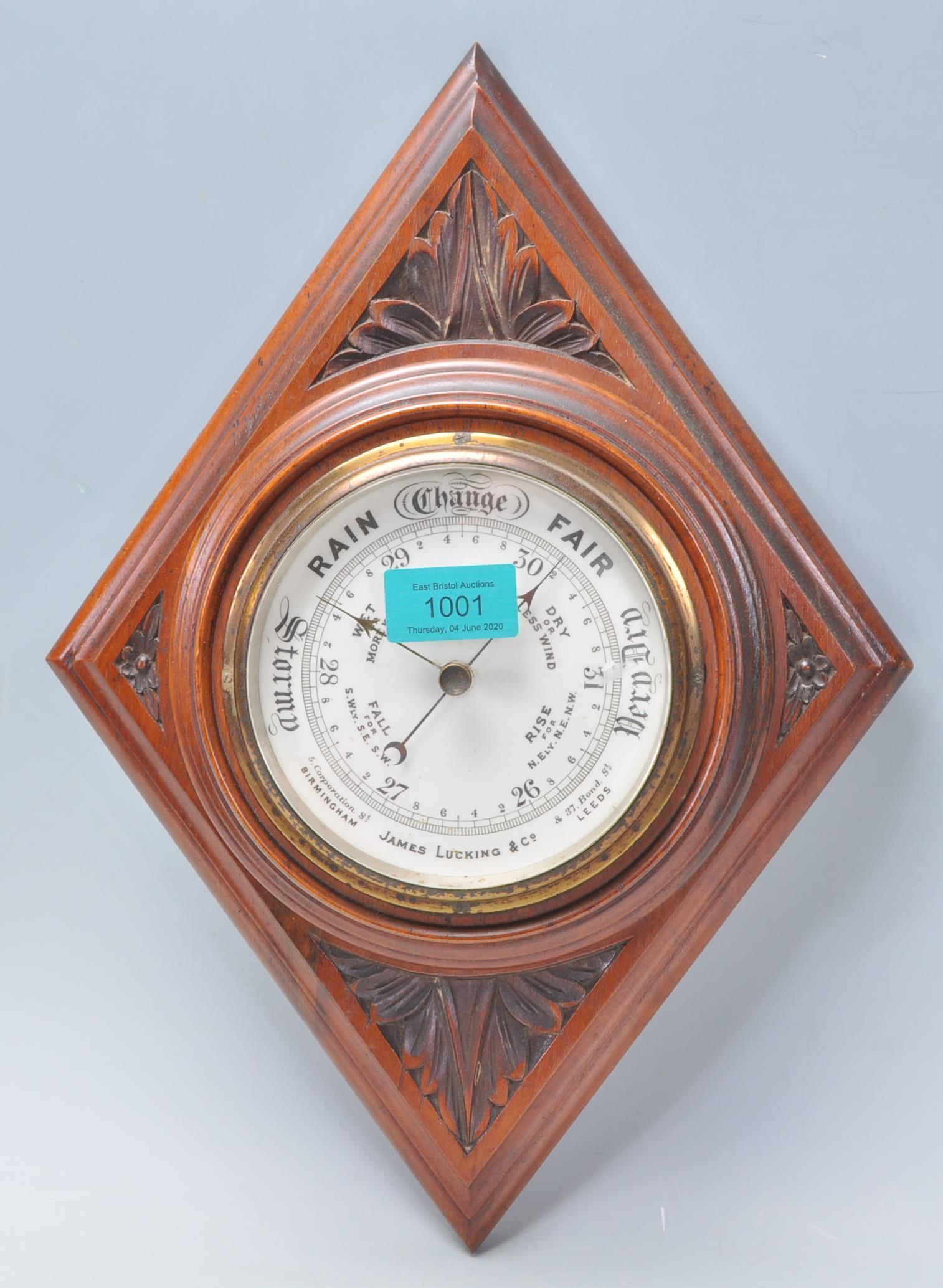 An early 20th Century carved oak barometer of lozenge shaped form having an enameled central round