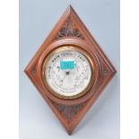 An early 20th Century carved oak barometer of lozenge shaped form having an enameled central round