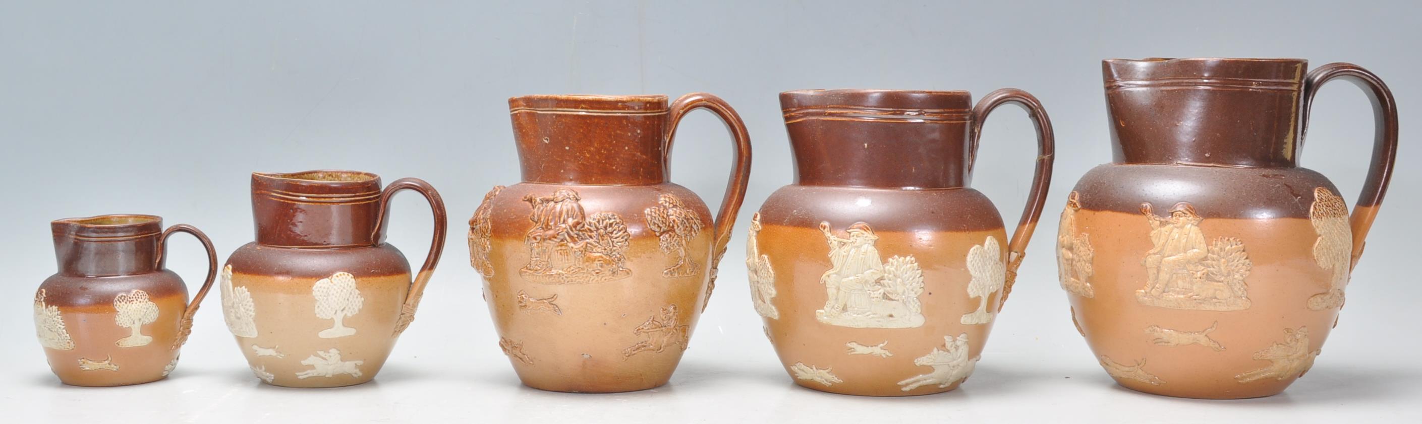 A group of five graduating 19th Century Doulton Lambeth stoneware jugs having applied raised white