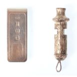 A silver whistle with bark effect detailing having illegible markings together with a silver