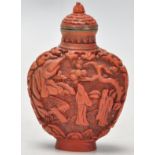 An Antique Chinese red cinnabar snuff bottle carved with landscape scenes and carved stopper atop.