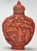 An Antique Chinese red cinnabar snuff bottle carved with landscape scenes and carved stopper atop.