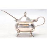 A hallmarked Sterling silver mustard pot set upon four figured feet with a hinged lid and finial