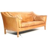 A vintage retro style two seater sofa settee having a wooden frame with tan brown leather upholstery