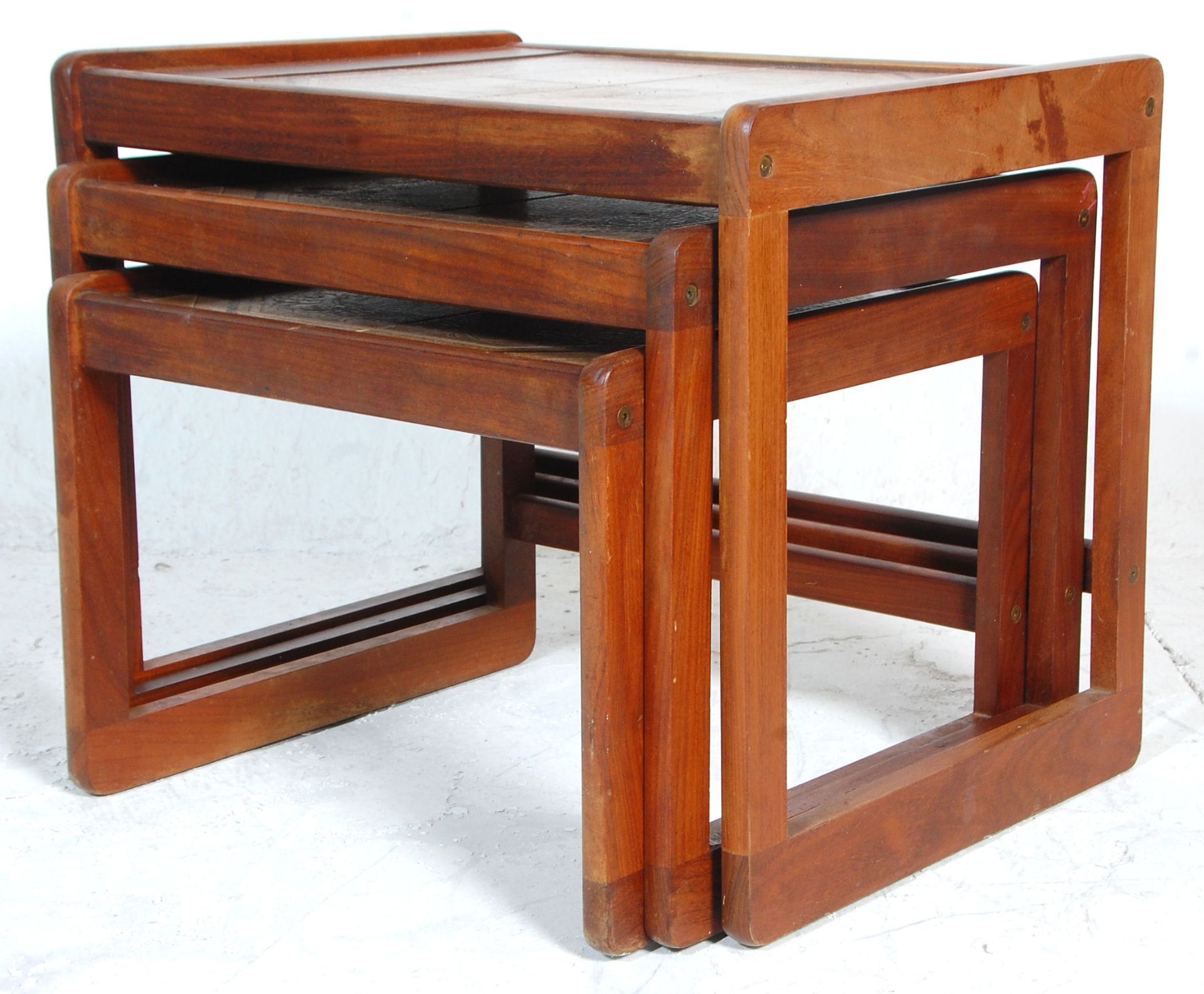 A 1970's Danish influence teak wood and tile top nest of graduating tables being raised on quadrille