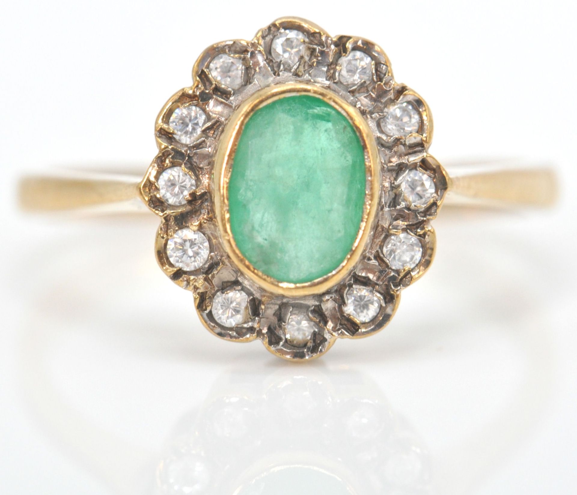 A hallmarked 9ct emerald and white stone cluster ring. The ring set with an oval mix cut emerald