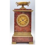 An early 20th Century red marble mantel clock of upright rectangular form having a brass urn atop