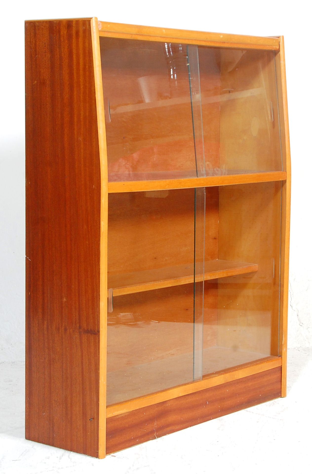 A vintage retro mid 20th Century bookcase having two shelves within, both having glass sliding doors