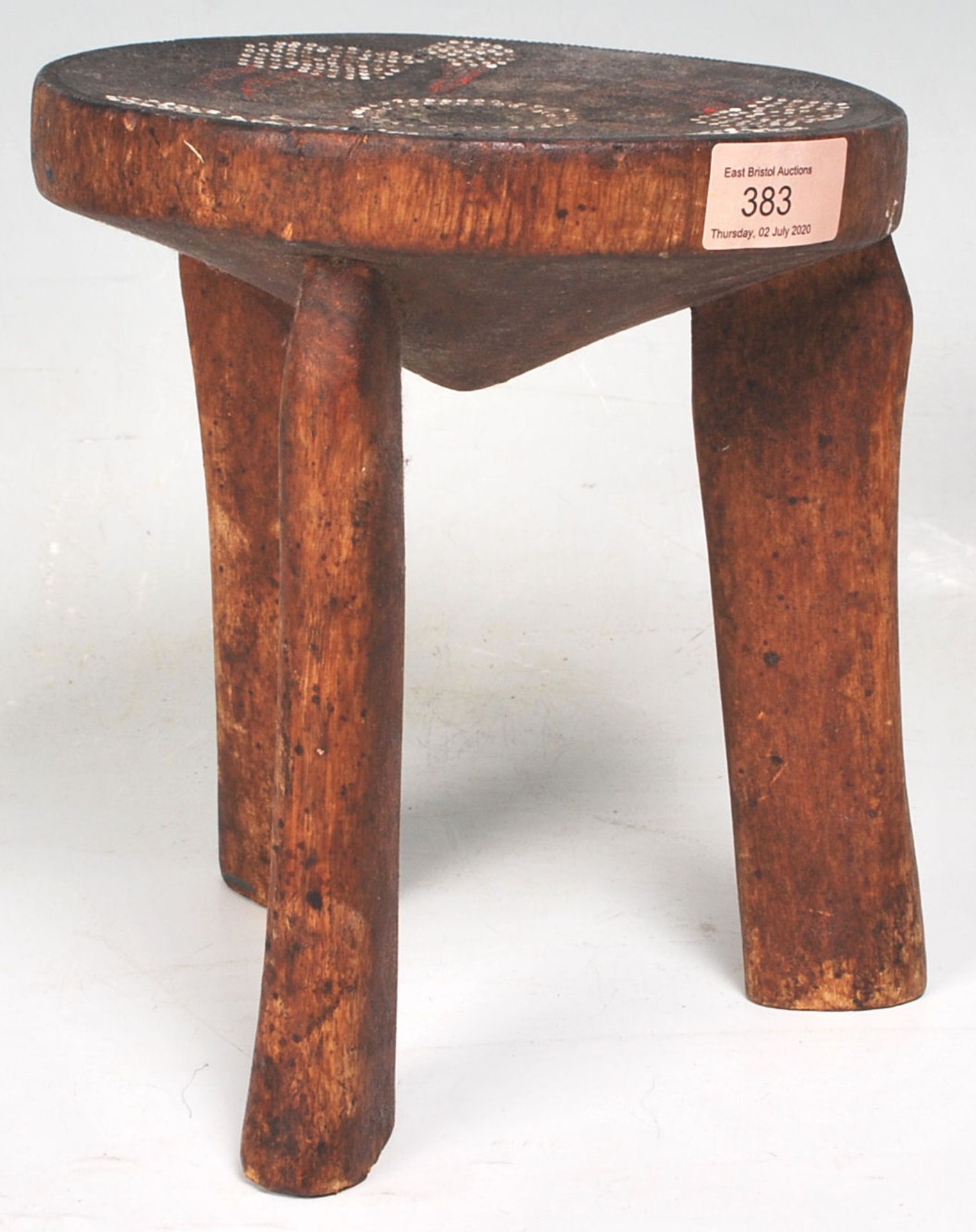 An Australian aboriginal wooden tribal stool having a around seat with three carved legs below,