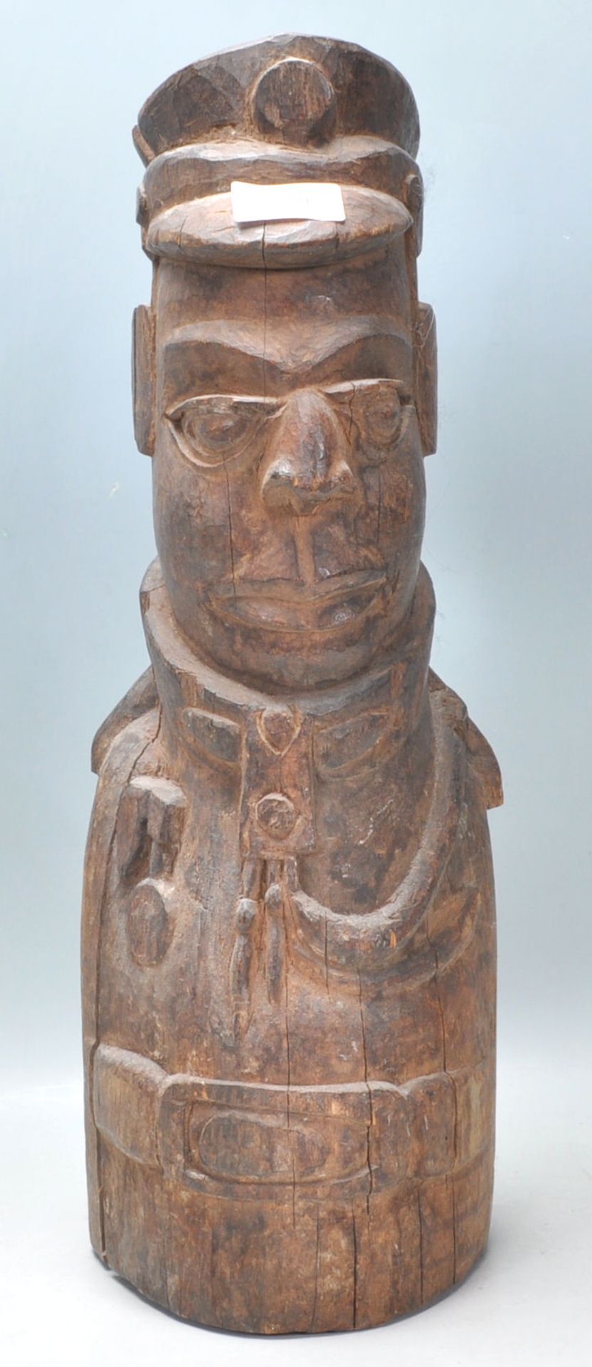 An unusual carved wooden African tribal figurine in the form of a uniformed officer, with cap to the