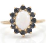 A 9ct gold hallmarked opal and sapphire cluster ring. The central oval cabochon within a halo of