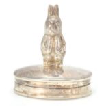 A silver hallmarked pill box of oval form having a small figure in the form of Peter Rabbit.