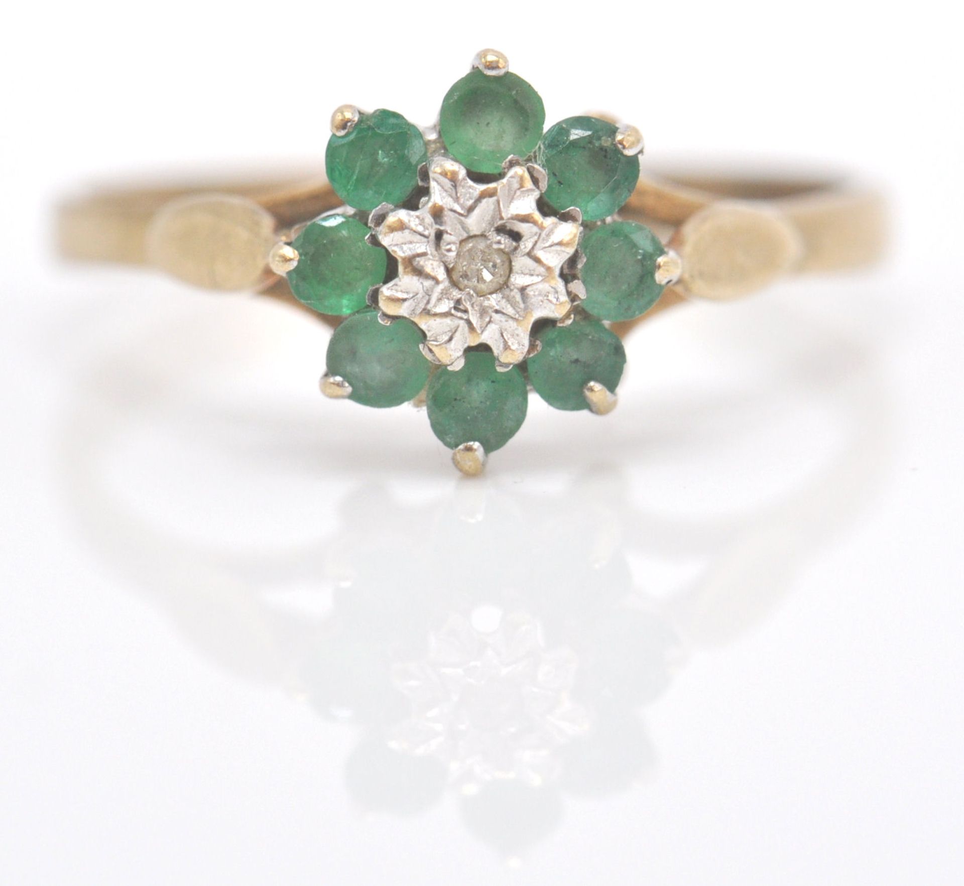 A 9ct gold emerald and diamond cluster ring. The ring with central  mixed cut diamond within a