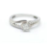 A 9ct white gold crossover ring having a central square cut diamond with white accent stones to