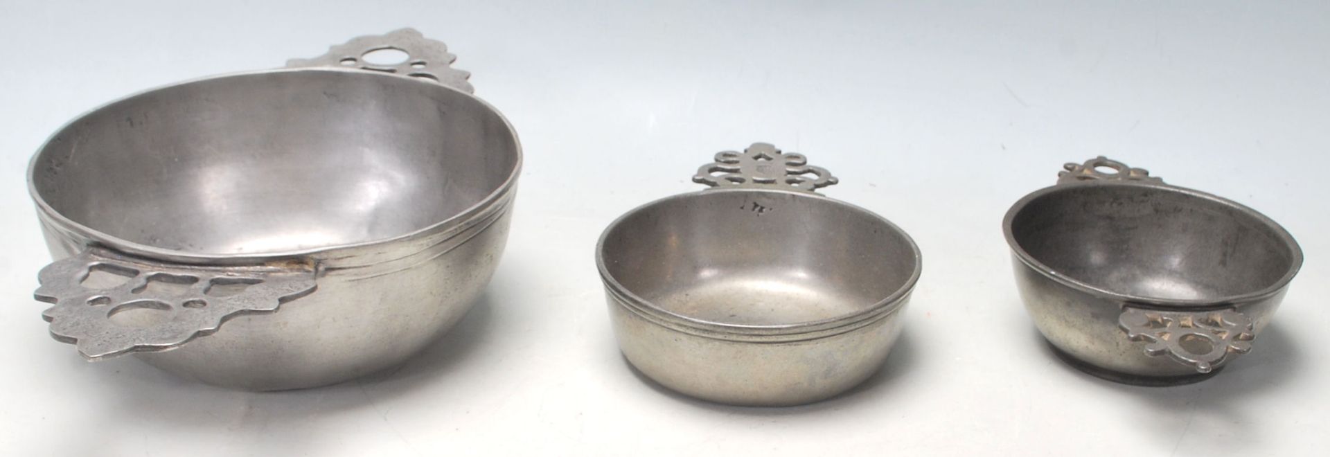 A collection of three early 20th Century pewter porringer / drinking bowls having pierced twin