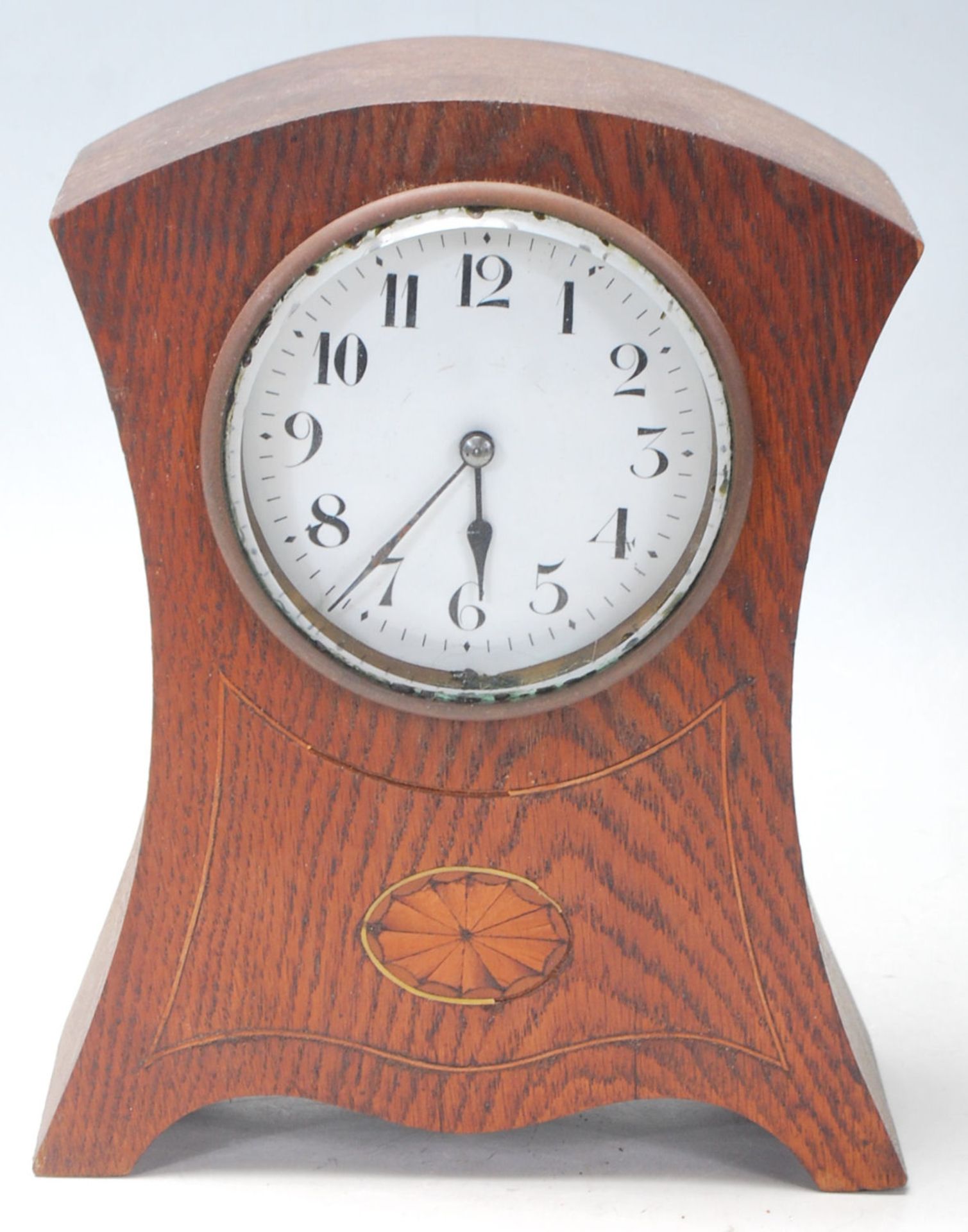 An early 20th Century French oak mantel / mantle clock having a round white enamelled face with