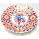 A 19th Century Japanese Imari charger plate with scalloped rim, typical decoration with a vase of