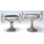 A pair of early 20th Century pewter twin handled vases raised on columnal supports with footed bases