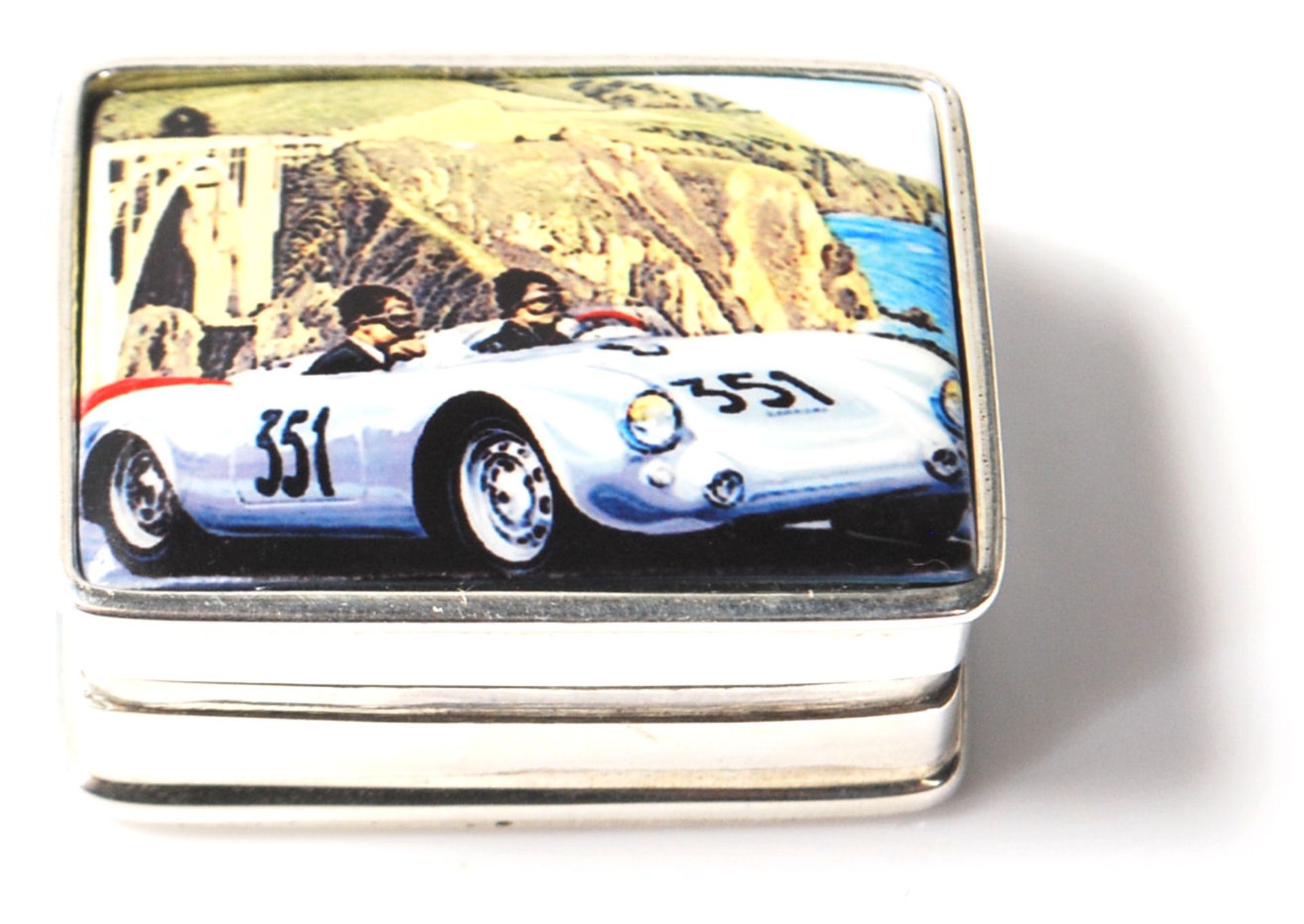 A silver and enamel pill box decorated with a Porsche 550. Weighs 20g. Measures 3cm.