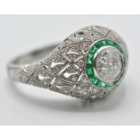 A platinum diamond and emerald ladies dress ring being set with a central round cut diamond with a
